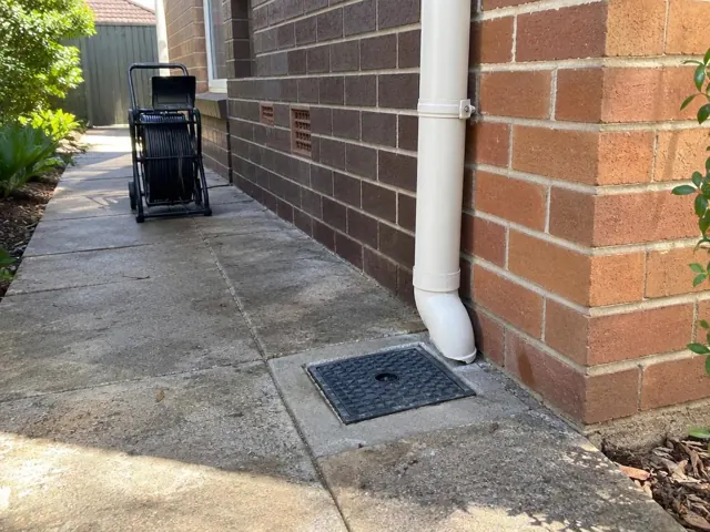 Capped drain inspection opening beside a brick house wall and concrete path in Normanhurst