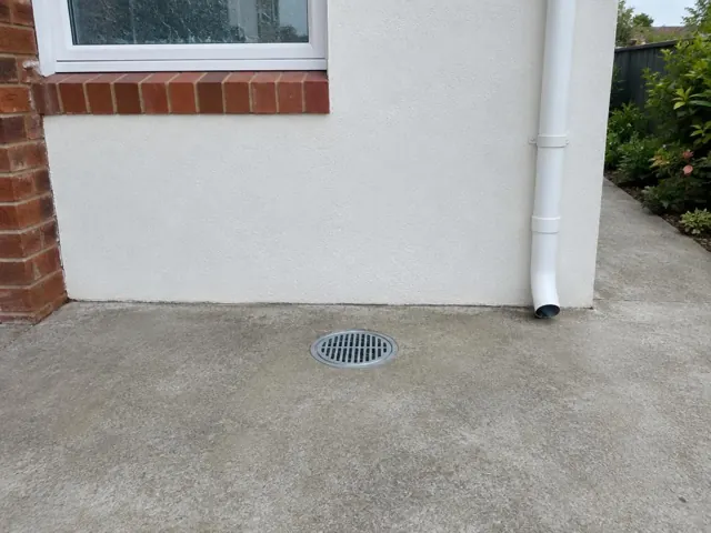 Outdoor grated gully beside a white rendered house wall and concrete paving in Pennant Hills
