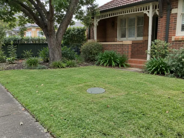 Lawn with a flush circular sewer cap beside a brick house and garden in Normanhurst